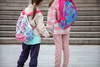 dos-ninas-hermosas-mochilas-espalda-van-escuela-juntas-mano-cerca-concepto-amistad-infantil_169016-8438